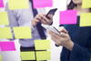 two people using their mobile phones in front of a wall of post-it notes